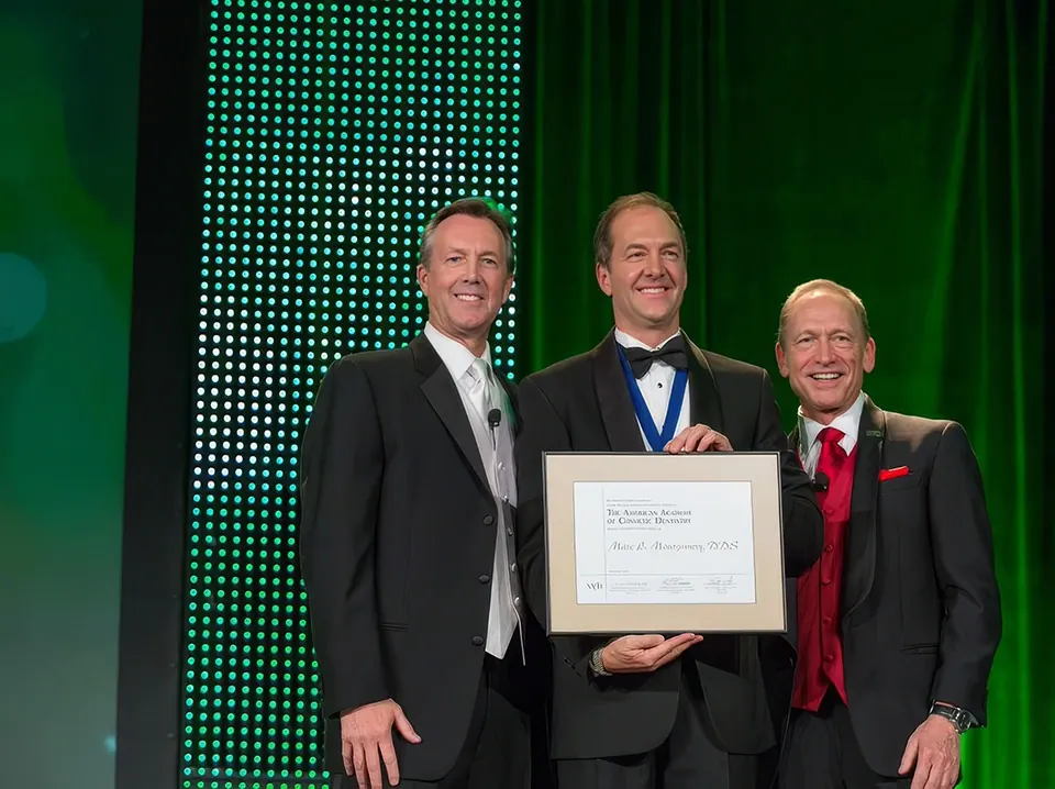 Dr. Marc Montgomery, center, on stage holding his American Academy of Cosmetic Dentistry certificate.
