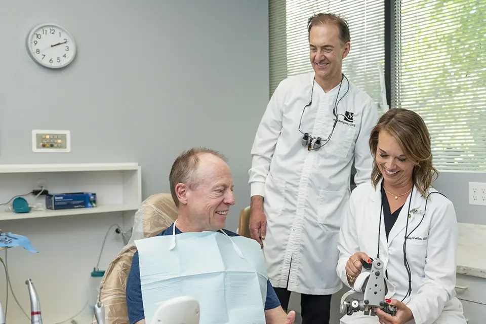 Dr. Marc Montgomery and Dr. Stacey Wolken with a smiling patient in a treatment room at Montgomery Wolken Dental Care, Woodbury.
