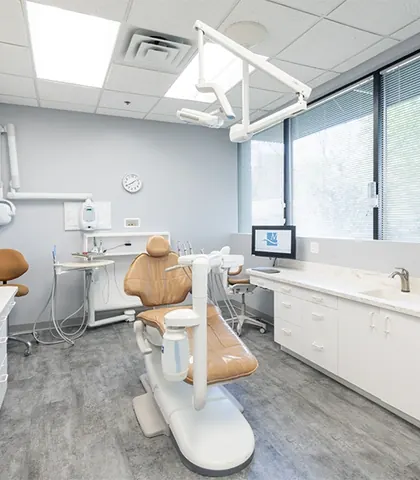 A bright treatment room with a window and a tan patient chair.